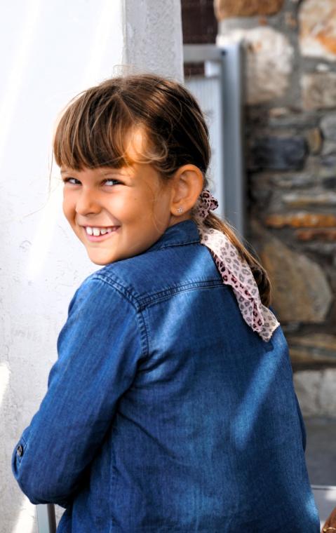 Bambina sorridente con camicia di jeans e fiocco nei capelli.